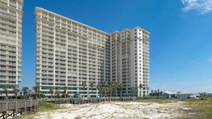 A high-rise hotel with multiple balconies, a beach view, and a wooden boardwalk.