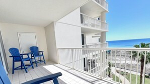 A balcony with white railings, a tiled floor, and blue chairs.