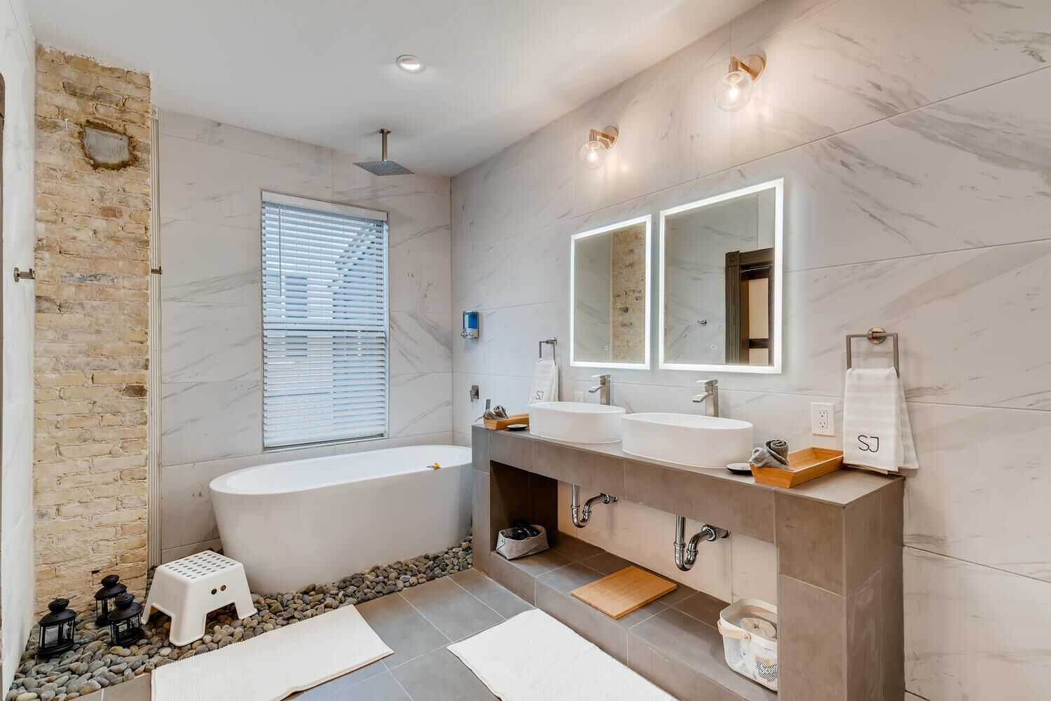 Un baño moderno con bañera, dos lavamanos, un espejo grande y un taburete pequeño.