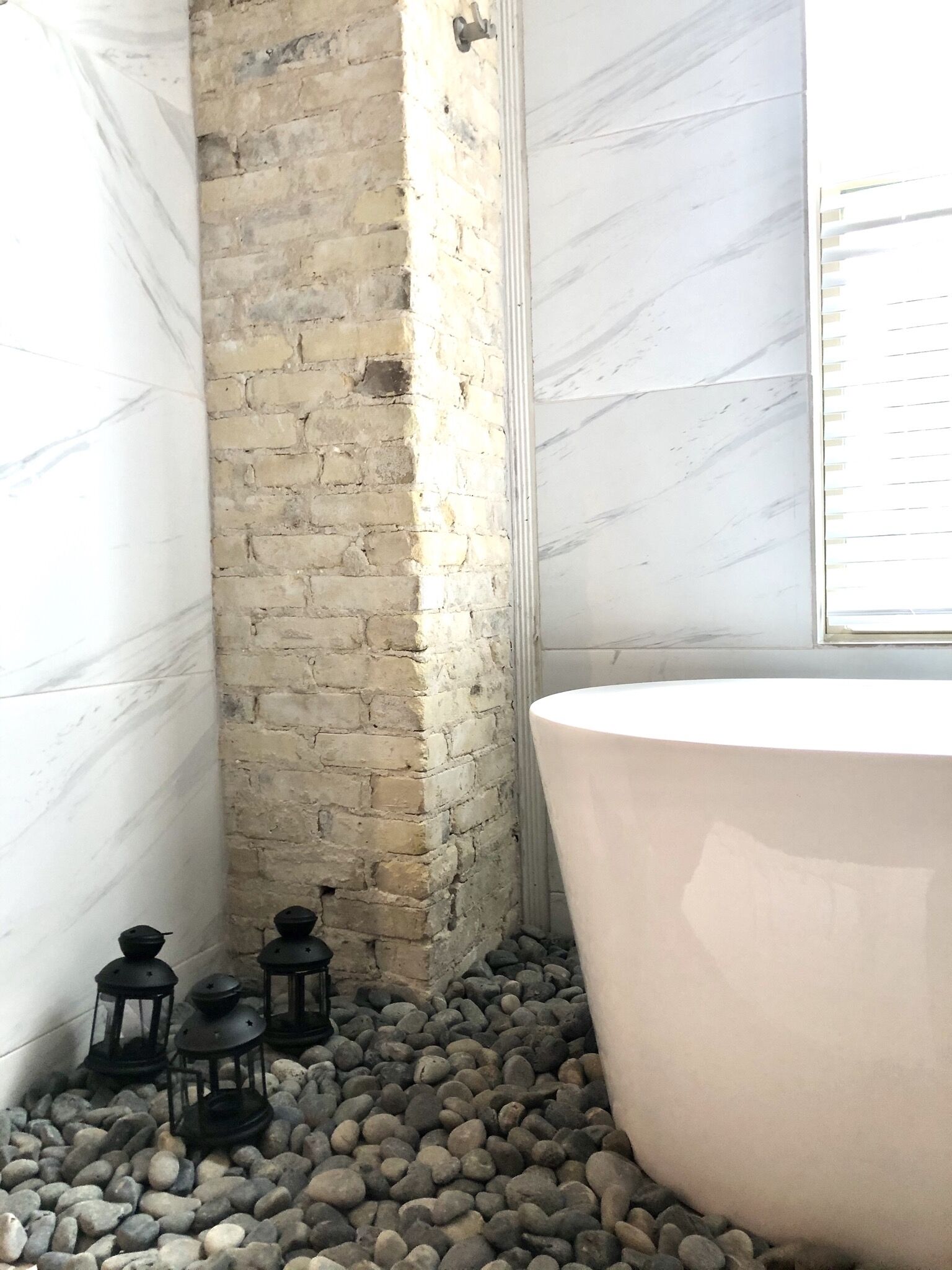 Un baño con una bañera grande, una pared de ladrillo y un suelo de mármol.