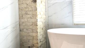 Un baño con una bañera grande, una pared de ladrillo y un suelo de mármol.