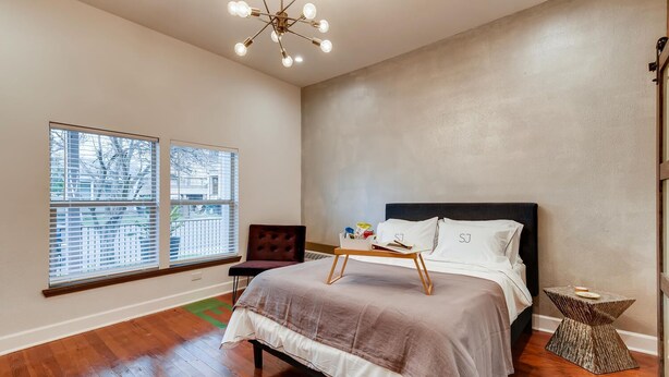 A bedroom with a bed, a chair, a bedside table, a window, and a chandelier.