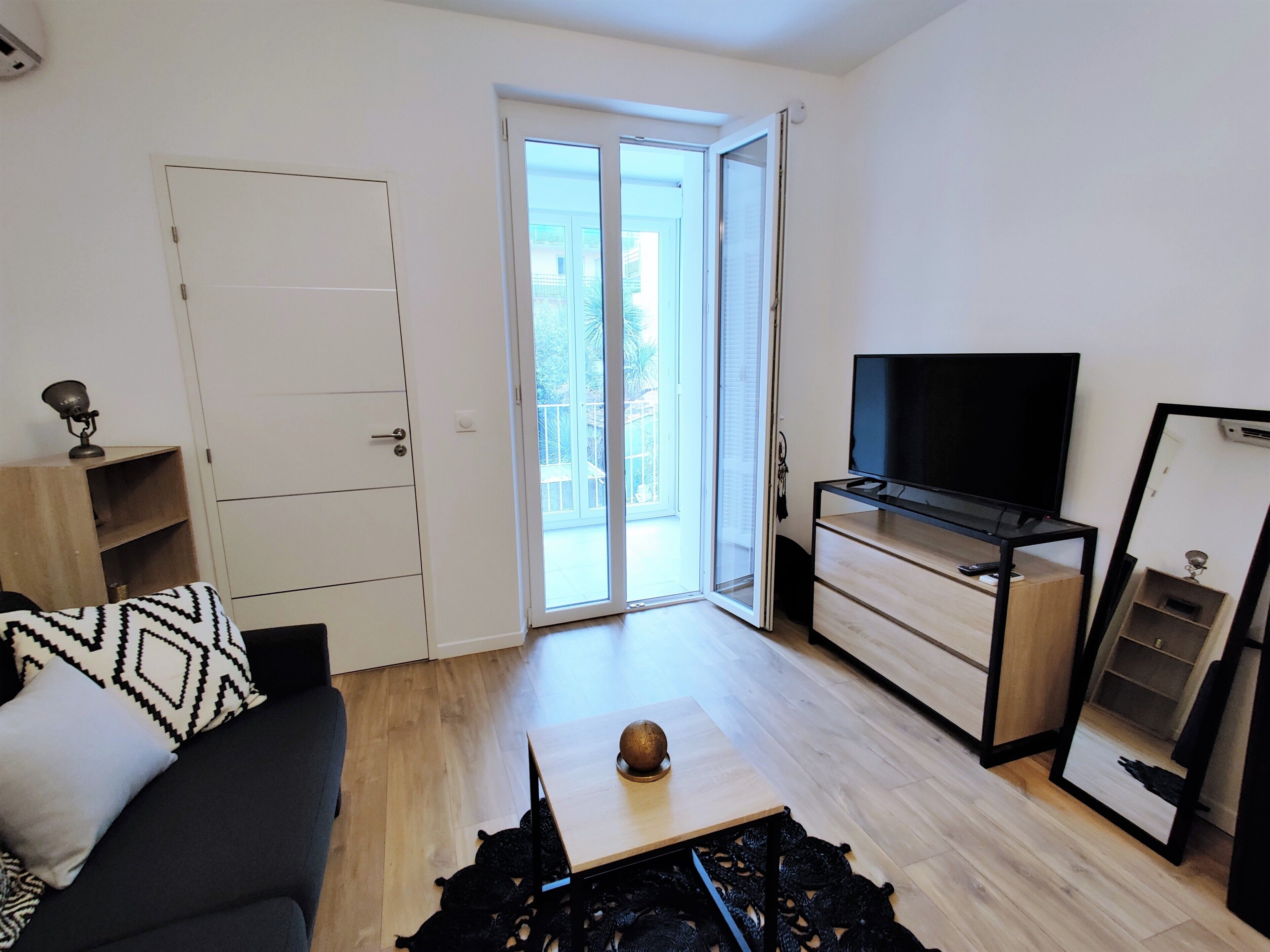 A modern living room with a sofa, a coffee table with a decorative item, a TV on a stand, and a sliding glass door leading to an outdoor area.
