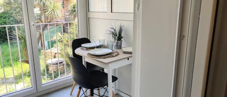 A balcony with a dining table set for two, featuring a potted plant and a glass.