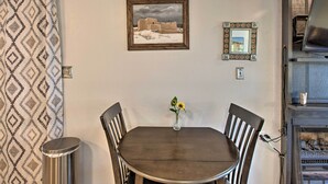 A dining area with a table and chairs, a framed picture on the wall, and a small vase with flowers. - Angel Fire Condo: Walk to Slopes & Trails! (Angel Fire)