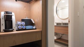 A compact kitchenette with a Keurig coffee maker, a coffee pod dispenser, and a small trash bin.