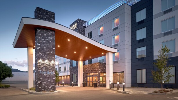 Una entrada de hotel moderna con fachada de piedra, ventanas amplias y un corredor cubierto.