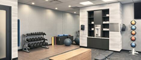 A gym with exercise equipment, a bench, and a wall-mounted dumbbell rack.
