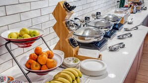 Mesa de buffet con tazones de frutas, un puesto de frutas y diversos utensilios de servicio.