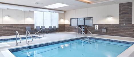 A swimming pool with a tiled edge, a sunroof, and a seating area with chairs and a table.