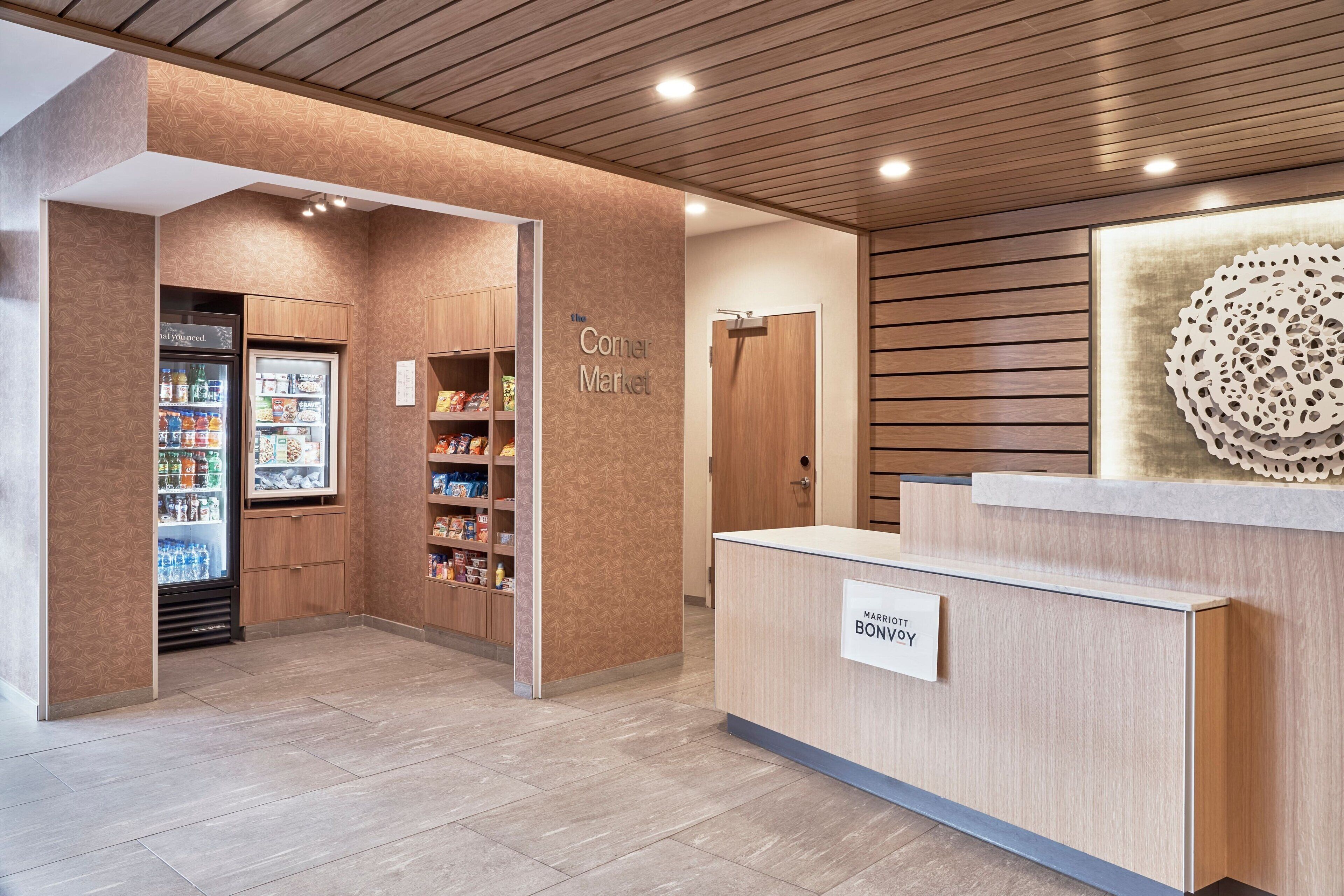A reception area with a wooden reception desk, a refrigerated display case, and a 'Corner Market' sign.