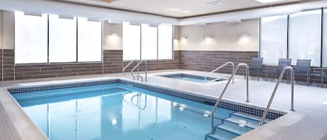 A large indoor swimming pool with clear blue water, surrounded by tiled walls and a brick accent wall.