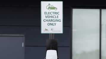 An electric vehicle charging station with a sign indicating it is for electric vehicles only, set against a building facade.