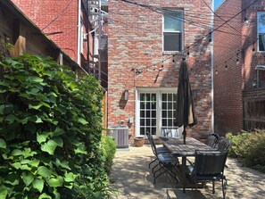 A brick building with a patio area featuring a table and chairs, a door, and a window.