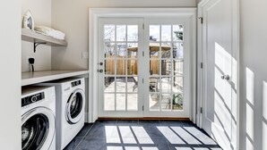 Un cuarto de lavandería con dos lavadoras, un tendedero y una puerta que da a un patio trasero con cerca de madera y mobiliario exterior.