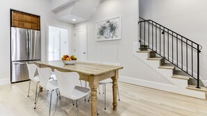 Una cocina moderna con un refrigerador de acero inoxidable, una mesa de comedor de madera con sillas blancas y una escalera con barandillas negras.