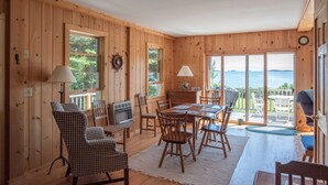 A wooden cabin interior with a dining area, checkered chairs, and a view of the outdoors.