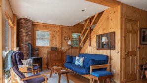 A cozy wooden cabin interior with a sofa, rocking chair, and fireplace.