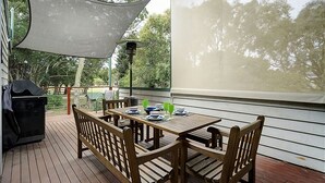 A covered patio with a wooden table and chairs, a grill, and a view of trees. - SOMETHING FOR EVERYONE (Somers)