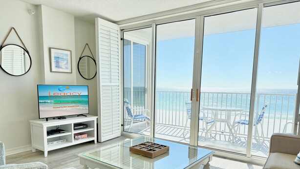 Ein Wohnzimmer mit einem Glastisch, weißen Sofas und einem Fernseher, der 'Legacy Vacations' anzeigt.