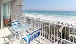 A balcony with a white railing, a glass table, and blue chairs overlooking a beach. - Island Princess 507 Amazing Views + Beach Service + Assigned Covered Parking! (Fort Walton Beach)