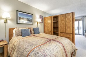 Une chambre avec un grand lit, une armoire en bois, un tableau encadré au mur et une table de chevet avec une lampe.