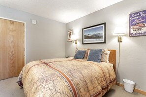 Une chambre à coucher avec un lit, un tableau encadré, une lampe fixée au mur et une porte en bois.