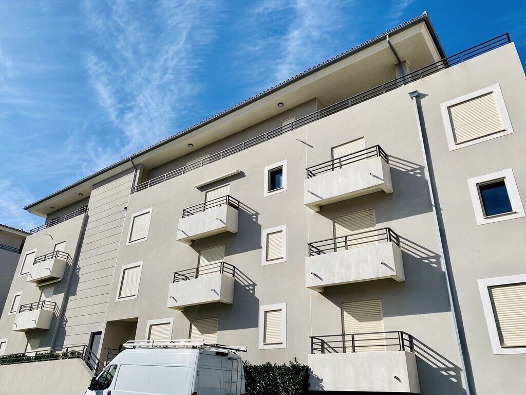 A multi-story residential building with balconies and a white van parked in front.