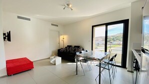 A modern apartment with a dining area, a sofa, a red ottoman, and a view of the city through large windows. - MARINA D'ORU - Comfortable studio in town center (M) (PROPRIANO)