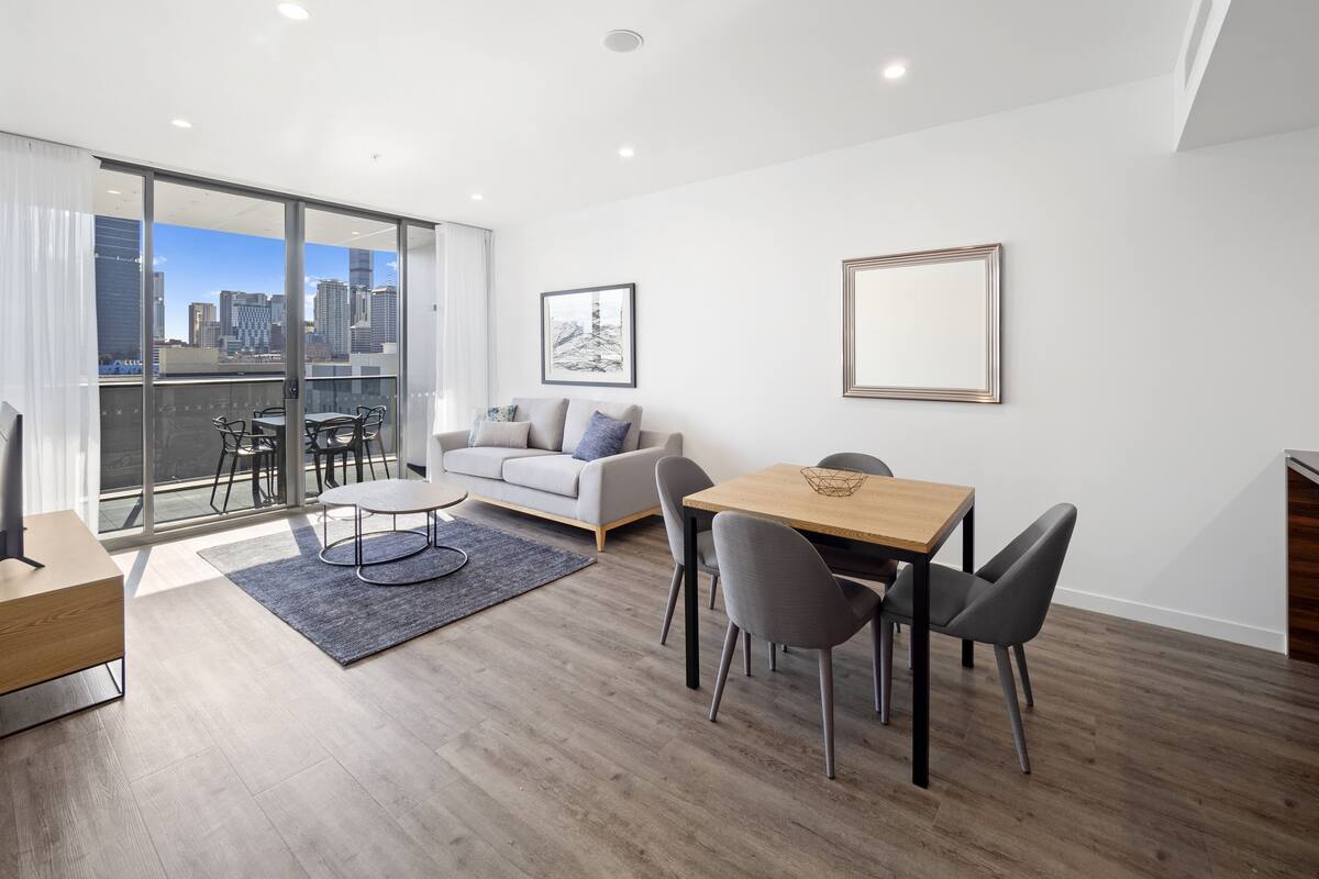Uma sala de estar moderna com sofá, mesa de jantar e cadeiras. Há uma janela grande com vista para a cidade.