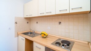A small kitchen with white cabinets, a sink, and a stove. There is a fruit basket on the counter.