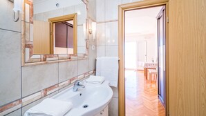 Ein Badezimmer mit einem Doppelwaschbecken, einem Spiegel und einer Holztür zu einem Flur.
