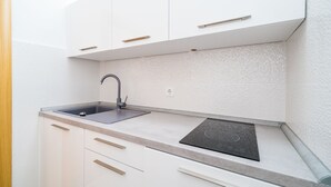 Eine moderne Küche mit weißen Schränken, einer Edelstahl-Spüle und einer schwarzen Induktionskochplatte.