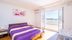 Ein Schlafzimmer mit Bett, Nachttisch und Meerblick durch eine Glastür.