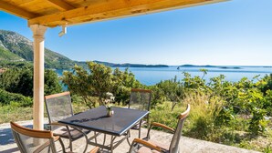 A covered outdoor seating area with a table and chairs, overlooking a scenic view of a lake and mountains. - Apartment Blue Chill - One-Bedroom Apartment (Mlini)