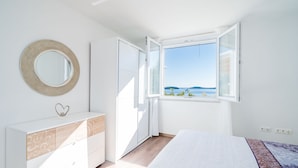 A bedroom with a bed, a dresser, a mirror, and a window with a view of the sea. - Apartment Blue Chill - One-Bedroom Apartment (Mlini)