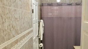 Een badkamer met marmeren tegels, een douchegordijn, een toilet en een prullenbak.