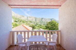 Ein Balkon mit Tisch und Stühlen, der einen Blick auf eine gebirgige Landschaft mit Häusern bietet.