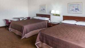 Une chambre d’hôtel avec deux lits, une petite table, une chaise et deux lampes fixées au mur.