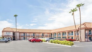 Un motel à plusieurs étages, avec un toit recouvert de tuiles, plusieurs voitures garées sur le parking et des palmiers.