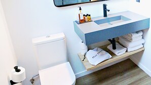 A bathroom with a white toilet, a sink with a mirror above it, and a shelf with towels and toiletries. - Lo Paller (Alt Aneu)