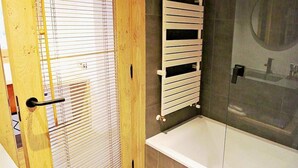 A bathroom with a bathtub, a wooden door with blinds, and a towel rack. - Lo Paller (Alt Aneu)
