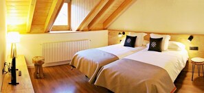 A room with two beds, wooden flooring, a radiator, a lamp, and a small stool.