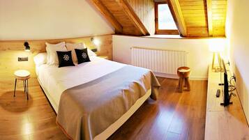 Un dormitorio acogedor con techo de madera, una cama grande con ropa blanca y almohadas decorativas, una mesita de noche pequeña, un radiador y suelo de madera.