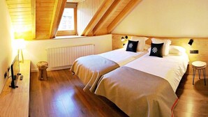A bedroom with two beds, wooden floors, a window, a radiator, and a small stool. - Lo Paller (Alt Aneu)