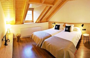A bedroom with two beds, wooden floors, a window, a radiator, and a small stool. - Lo Paller (Alt Aneu)