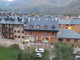 Un hotel de varios pisos, con fachada de piedra y un letrero que indica que es un hotel. Hay coches estacionados en la entrada.