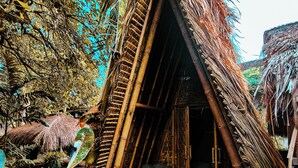 Una cabaña con techo de paja y estructura de bambú tejido, rodeada de follaje tropical.