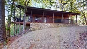 Une cabane en rondins avec des fondations en pierre, une terrasse en bois et une allée gravillonnée.