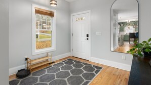 A hallway with a wooden bench, a gray rug, a white door, and a mirror reflecting a kitchen area.